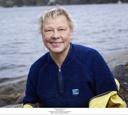 Porträttfoto av Inger Näslund med klippor och vatten i bakgrunden.