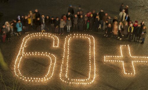 Folk samlade bakom ljusarrangemang där tända ljus formar texten "60+" på en kullerstensyta.