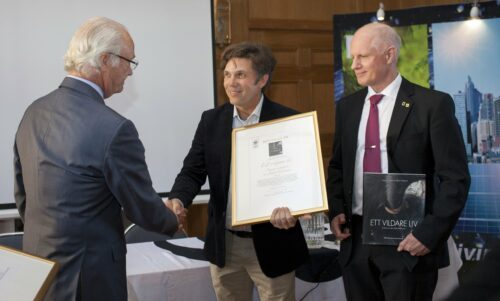 Magnus Lundgren och Staffan Widstrand tar emot pris av kung Carl XVI Gustaf. En av pristagarna håller ett inramat diplom och skakar hand med kungen medan den andra håller en bok med titeln "Ett vildare liv"