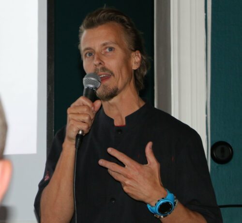 Paul Svensson talar i mikrofon och pekar mot bröstet med vänster hand.