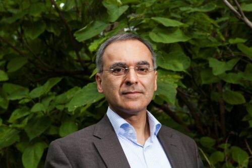 Porträttfoto av Pavan Sukhdev framför en bakgrund av gröna blad.