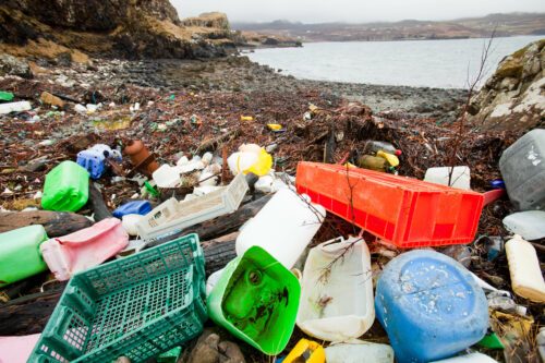 Strand täckt av färgglad plastskräp: trasiga lådor, dunkar, kassar och andra plastbehållare bland tång på stenig kust.