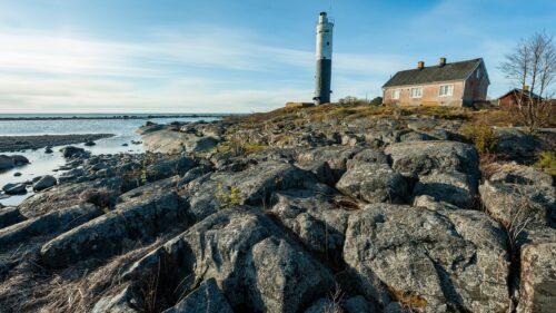 Klippkust med stora granitblock, en fyr och ett ensligt hus vid havet.