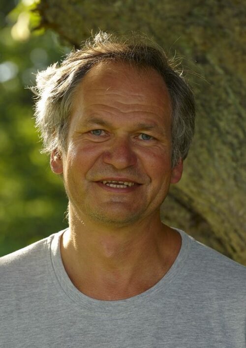 Porträttfoto av Peter Westman, lätt leendes mot kameran med en trädstam och grönska bakom sig.