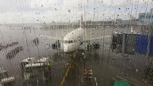 Regndroppar på fönstret, utanför syns ett suddigt flygplan ståendes vid en flygplansgate med jetbridge.
