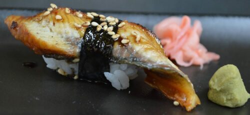 Nigiri med unagi (grillad ål) på ris, inlindad med nori, toppad med sesam, serverad med inlagd ingefära och wasabi.