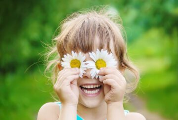 En leende flicka som håller två blommor för ögonen