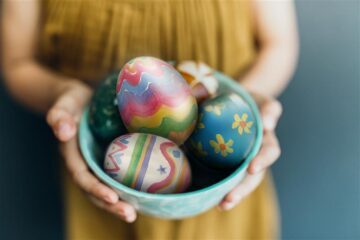 En skål med målade ägg hålls fram av en person klädd i gult