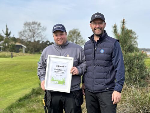 Två män på en golfbana. Den ena har mottagit ett diplom