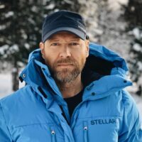 John Crawford från Stellar Equipment står framför snötäckta träd, iklädd en blå vinterjacka och mörkblå keps, och tittar rakt in i kameran.