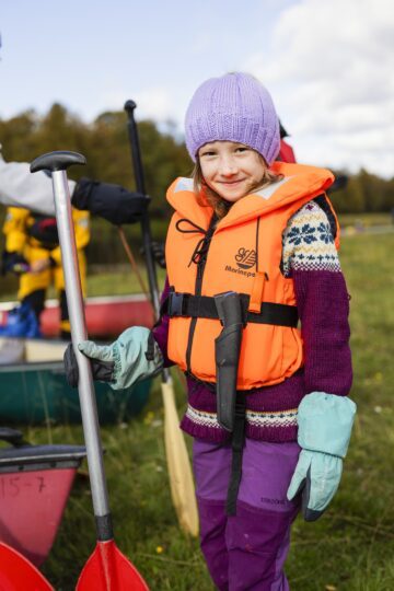 En flicka med flytväst håller i en paddel.