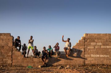 Children perch on the damaged wall outside the community