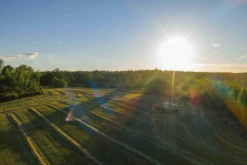 Flygfoto över Ogestad Egendom och Hyllela gård, Västerviks kommun, Småland, Sverige. Solen står lågt över träden och en skördetröska kör på ett fält
