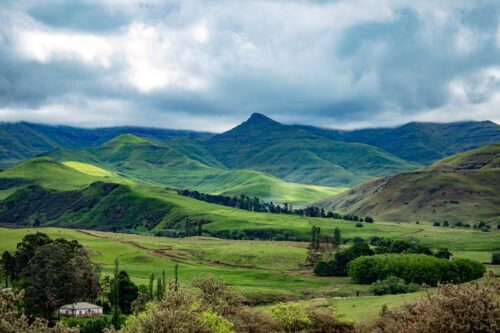 Berg med gröna kullar omgivna av frodiga ängar under molnig himmel.