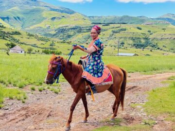 En kvinna rider på en häst, berg och gröna landskap syns i bakgrunden