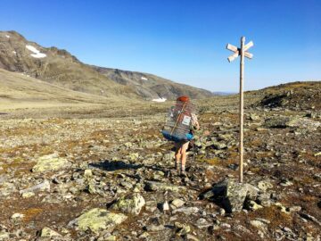 En person går på fjället, med en bur på ryggen.