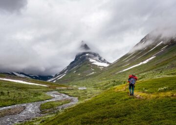 En person vandrar över fjället på sommaren. Berg och tjocka moln syns i bakgrunden.