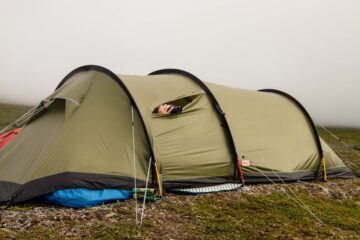 Grönt tält, i ett litet hål ser man någons händer, som håller en kikare och verkar titta ut.