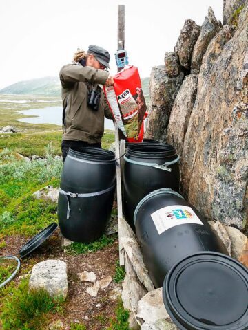 En person fyller på svarta tunnor med hundmat.