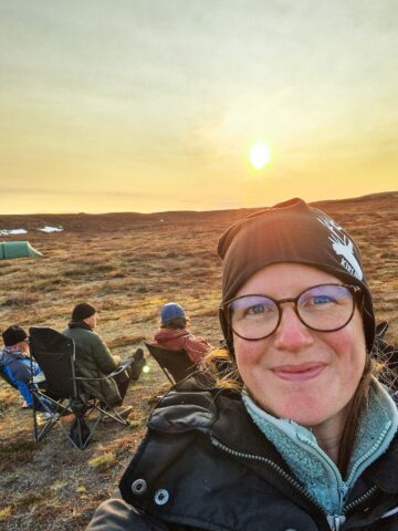 Therese Wåtz leendes mot kameran, bakom syns en solnedgång och två personer sittandes i stolar.