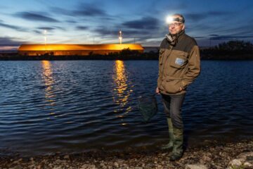 Foto av biologen Mats Wirén, ståendes med en pannlampa på sig vid ett vattendrag på kvällen.