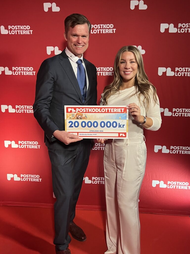 WWF Sveriges generalsekreterare Gustaf Lind poserar tillsammans med WWF-ambassadören Therese Lindgren. De håller tillsammans upp en check från Postkodlotteriet som visar att lotteriet år 2026 delat ut 20 miljoner till WWF.