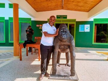 Paul Hatanga står bredvid en bergsgorillestaty.