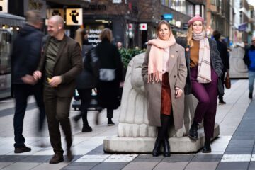 Maria Soxbo och Emma Sundh, grundare av Klimatklubben. De står sida vid sida, lutandes mot ett betonglejon på drottninggatan. Flera människor syns gåendes förbi dem.